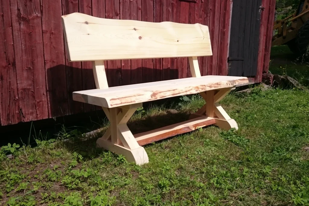 Vacker träbänk med ryggstöd från Nordanlids Rustik. En fin design och variant på kryssben. Trädets naturliga former är sparade på vissa kanter.